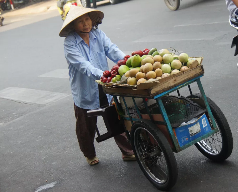 Vietnamese lady pushing a cart full of fruit on the streets of Saigon, Vietnam in Ho Chi Minh City. 
