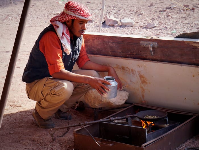 A Bedouin man in traditional clothing roasting coffee beans to make coffee in the dessert during our eco experience in Jordan