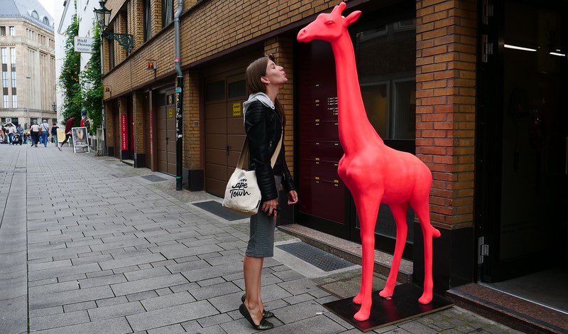 A giant giraffe sculpture outside in Dusseldorf, Germany with That Backpacker Audrey Bergner posing tall beside it