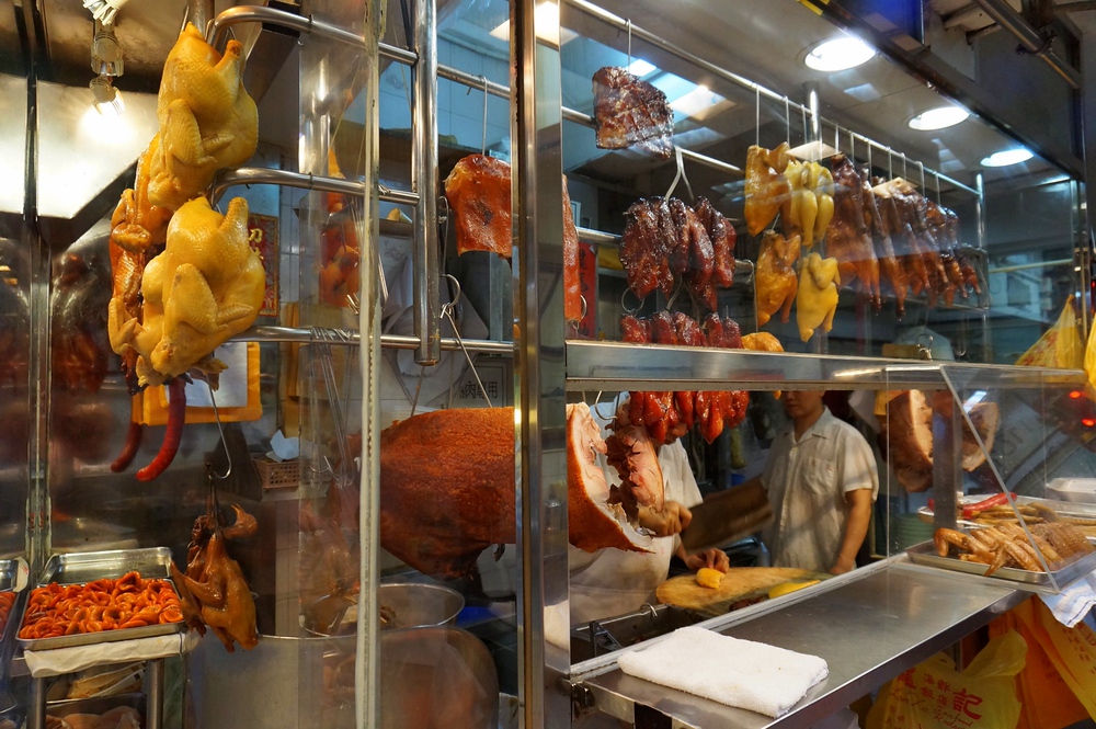 A roasted meat shop with chickens, geese, ducks, and pork hanging from the window of a butcher on the streets of Hong Kong 