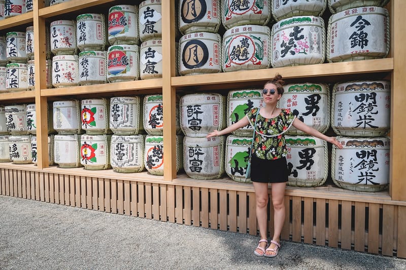 A wall of sake offerings on our day trip to Kamakura with That Backpacker Audrey Bergner showcasing it and showing how small she is next to the display case A wall of sake offerings on our day trip to Kamakura with That Backpacker Audrey Bergner showcasing it and showing how small she is next to the display case