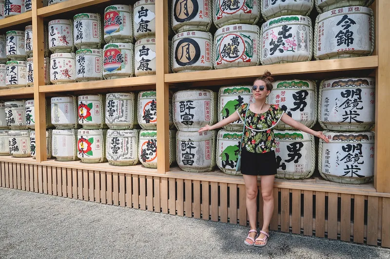 A wall of sake offerings on our day trip to Kamakura with That Backpacker Audrey Bergner showcasing it and showing how small she is next to the display case A wall of sake offerings on our day trip to Kamakura with That Backpacker Audrey Bergner showcasing it and showing how small she is next to the display case