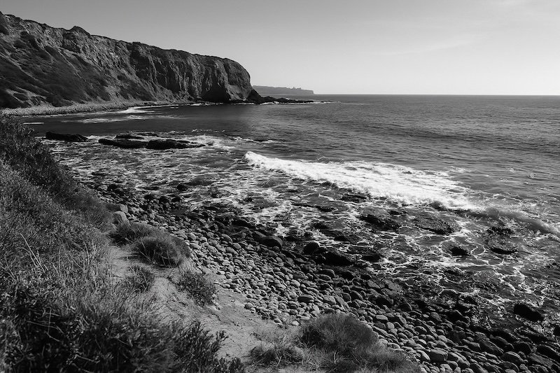 A black and white photograph of Abalone Cove Shoreline Park in Palos Verdes, California. Rugged cliffs line the coast, with waves breaking gently on rocky shores. Coastal vegetation frames the scene, and the Pacific Ocean extends to the horizon under clear skies A black and white photograph of Abalone Cove Shoreline Park in Palos Verdes, California. Rugged cliffs line the coast, with waves breaking gently on rocky shores. Coastal vegetation frames the scene, and the Pacific Ocean extends to the horizon under clear skies