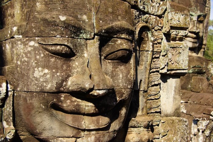 Close-up of an intricately carved stone face at the Temples of Angkor in Cambodia, showcasing the ancient Khmer artistry and weathered details of the sandstone sculpture