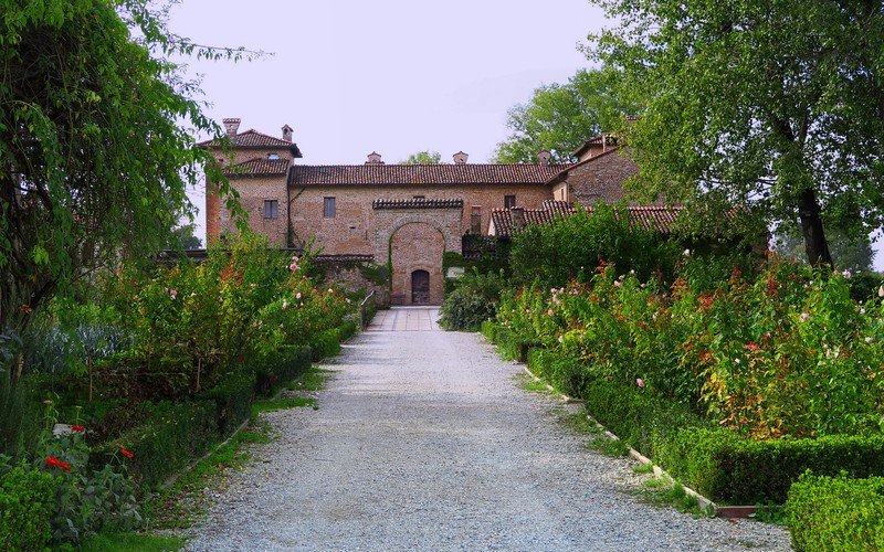 Tree-lined gravel pathway leading to Antica Corte Pallavicina, a historic estate in Emilia-Romagna, Italy, renowned for its elegant gardens, rustic architecture, and culinary heritage, offering travelers a glimpse into traditional Italian food culture