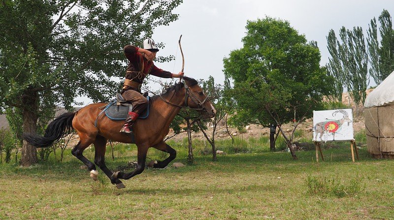 Archery on horseback demonstration in Bokonbayevo in Kyrgyzstan with a man on shooting at arrow at a target 