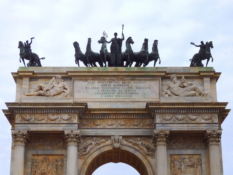 Close-up view of the Arco della Pace in Milan, Italy, highlighting its ornate neoclassical architecture, detailed stone carvings, and the bronze chariot sculpture with six horses atop the arch