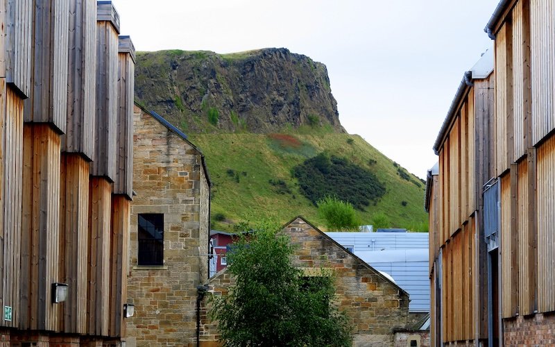 View of Arthur’s Seat from Edinburgh’s Old Town framed by modern wooden buildings and historic stone architecture during Eat Walk Edinburgh food tour