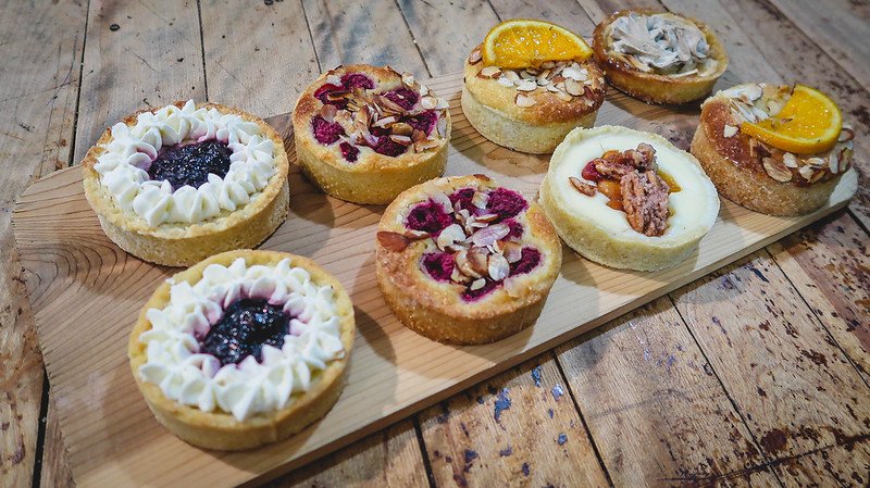 An assortment of artisanal tarts and pastries with vibrant toppings like berries, citrus, and nuts displayed on a wooden board at La Rumeur Affamée in Sutton, Quebec, showcasing the gourmet treats of the Eastern Townships.