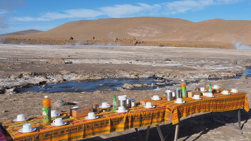Colorful picnic tables set for lunch overlooking the steaming geothermal fields near El Tatio Geysers in the Atacama Desert, Chile