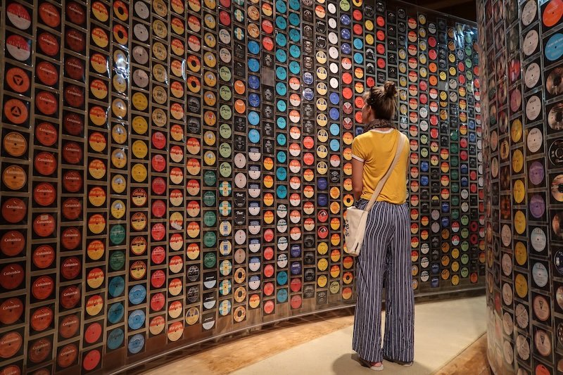 That Backpacker Audrey Bergner admiring a vibrant wall of colorful vintage vinyl records at the Cape Town museum, showcasing South Africa’s rich musical heritage in a striking art installation