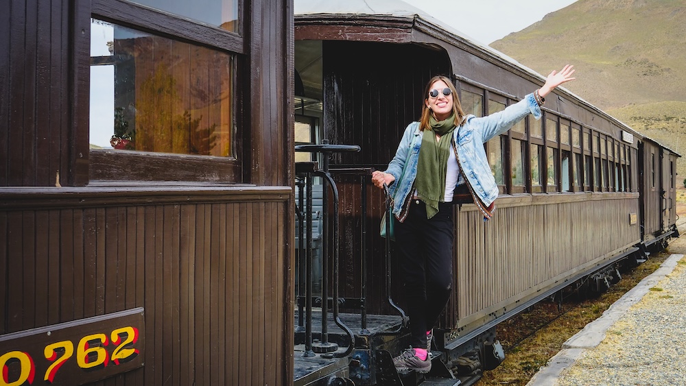 Audrey Bergner of That Backpacker waving from the vintage wooden car of La Trochita (the Old Patagonian Express) during a historic steam train journey in Esquel, Patagonia, Argentina.