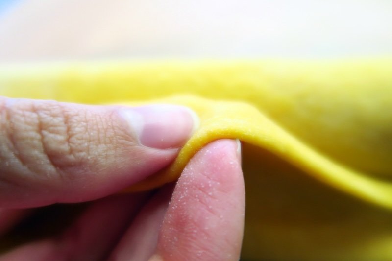 Close-up macro of Audrey Bergner of That Backpacker pinching thinly rolled fresh pasta dough during a cooking class at Casa Artusi in Emilia-Romagna, Italy, highlighting the hands-on techniques and authentic culinary traditions of Italian food culture