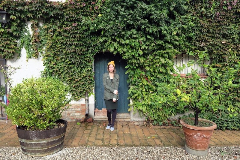 Audrey Bergner of That Backpacker standing in front of a rustic ivy-covered doorway at an agriturismo in Emilia-Romagna, Italy, capturing the charm of countryside travel and the region’s welcoming rural hospitality for food and culture lovers