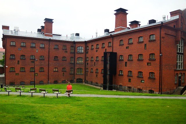 Audrey Bergner of That Backpacker sitting on a bench outside Hotel Katajanokka, Helsinki’s historic red-brick jail converted into a luxury hotel, capturing the unique blend of history, architecture, and modern hospitality in Finland’s capital city