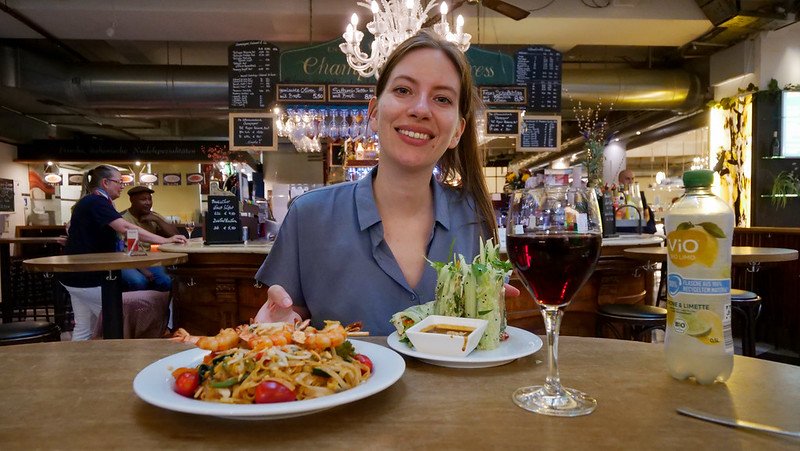 Audrey Bergner from That Backpacker enjoying a meal with pasta, salad, and wine at Markthalle Freiburg in Freiburg im Breisgau, Germany during a city food tour