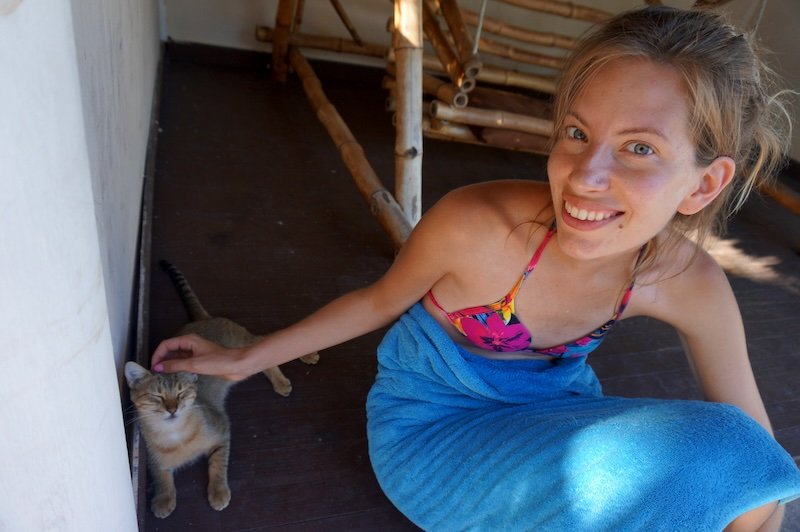 Audrey Bergner of That Backpacker smiling in a colourful swimsuit and wrapped in a blue towel while petting a friendly cat during her honeymoon in Cayo Santa María, Cuba