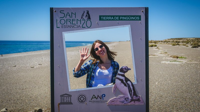 Audrey Bergner of That Backpacker poses playfully at the San Lorenzo Estancia photo frame, surrounded by the arid coastal landscape of Península Valdés in Patagonia, Argentina — a UNESCO World Heritage Site famous for its Magellanic penguin colonies