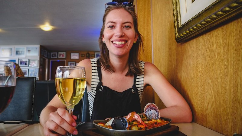 Audrey Bergner of That Backpacker smiling at a local restaurant in Puerto Madryn, Patagonia, enjoying a fresh seafood feast with a glass of white wine, showcasing Argentine coastal cuisine and the culinary highlights of Peninsula Valdes region