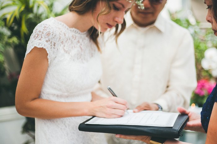 Audrey Bergner of That Backpacker signs the marriage certificate during her wedding to Nomadic Samuel in Brampton, Ontario. Captured inside a lush tropical greenhouse venue, this moment symbolizes the official start of their new life together