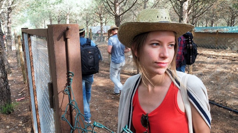 Audrey Bergner of That Backpacker wearing a sunhat, red dress, and light sweater draped over her shoulders while exploring La Vinyeta winery in Costa Brava, Spain, showing a stylish yet practical outfit choice for grape stomping and vineyard tours