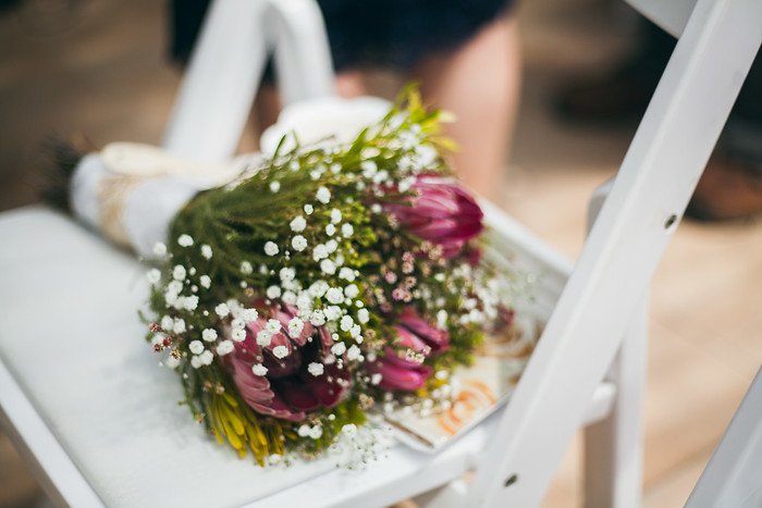 Close-up of Audrey Bergner’s wedding bouquet featuring vibrant South African proteas, delicate baby’s breath, and exotic greenery, resting on a white chair during the summer ceremony of Samuel and Audrey Jeffery in Brampton, Ontario