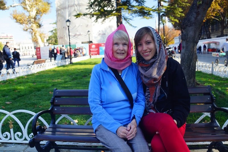 That Backpacker Audrey Bergner and Nomadic Samuel’s mom sitting on a park bench near Sultanahmet in Istanbul, Turkey, both wearing headscarves as a sign of respect before visiting a mosque