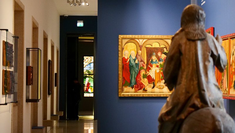 Colorful medieval panel paintings and stained glass displayed in a quiet gallery hall at the Augustiner Museum in Freiburg im Breisgau, Germany, highlighting religious art from Freiburg Cathedral.