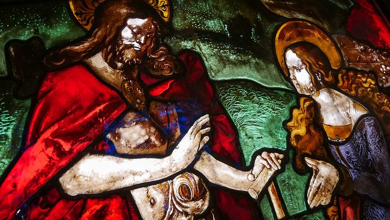 Close-up of a vibrant medieval stained glass window at the Augustiner Museum in Freiburg im Breisgau, Germany, depicting richly detailed religious figures in red, green, and gold hues