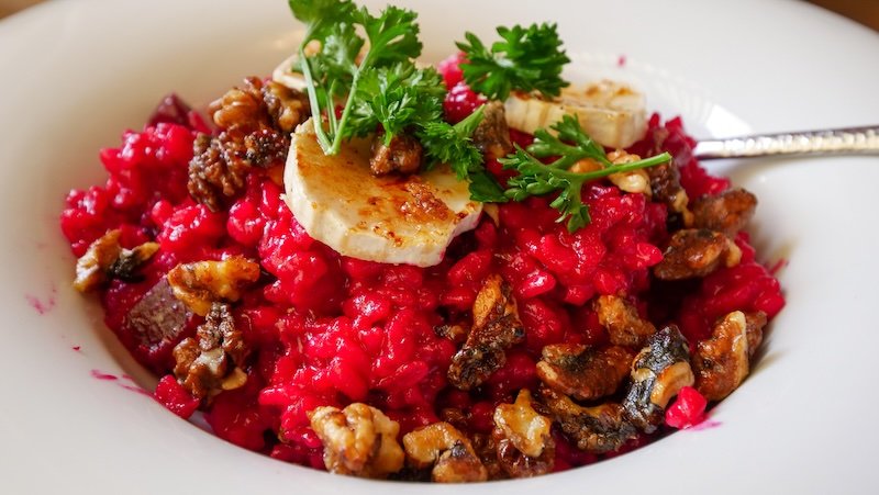Vibrant beetroot risotto served in Freiburg im Breisgau, Germany, topped with creamy goat cheese medallions, caramelized walnuts, and fresh parsley for garnish
