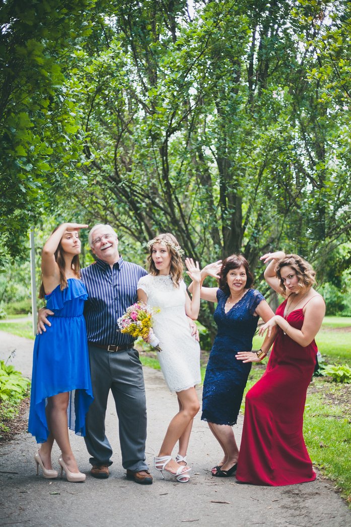 Playful Bergner family wedding portrait featuring Audrey Bergner in her lace dress with flower crown, holding a colorful bouquet, surrounded by family members in vibrant attire striking fun poses during Samuel and Audrey’s summer wedding in Brampton