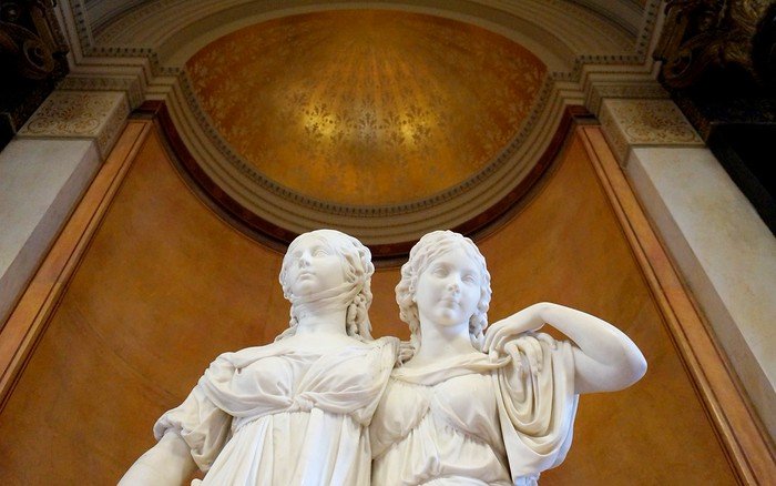 Marble statue of two women inside a Berlin museum, set against an ornate golden dome and decorative interior, highlighting the city’s rich collection of classical art and sculptures found while museum hopping in Germany’s capital
