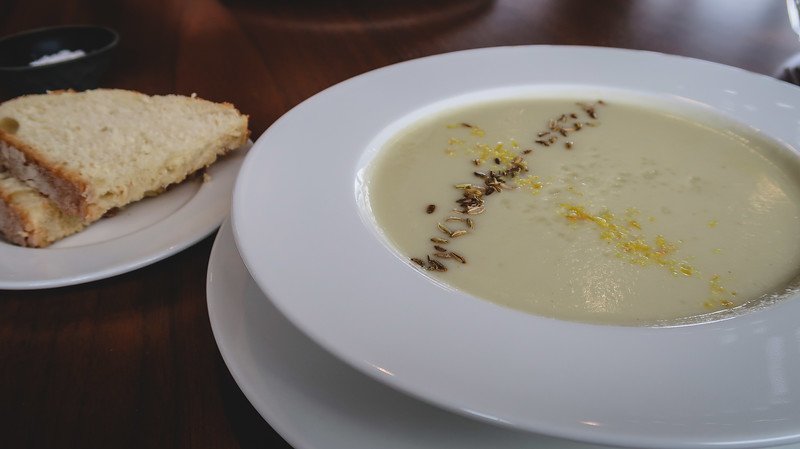 Creamy soup garnished with herbs and lemon zest served at the Blavatnik Building restaurant in Tate Modern, London, accompanied by fresh bread on the side, highlighting the refined dining experience within the museum’s modern setting