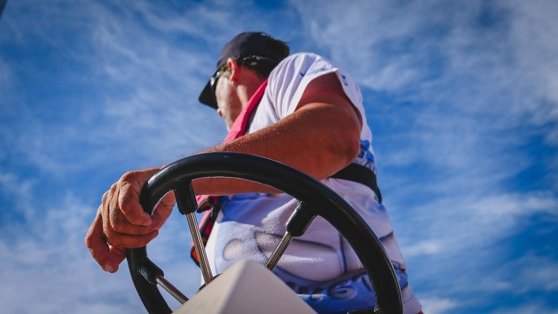 Close-up view of the boat captain steering the vessel during a wildlife boat tour from Puerto Pirámides, Península Valdés, Patagonia, Argentina. The shot, framed dramatically against a blue sky, captures the adventure of heading out to see sea lions and seabirds