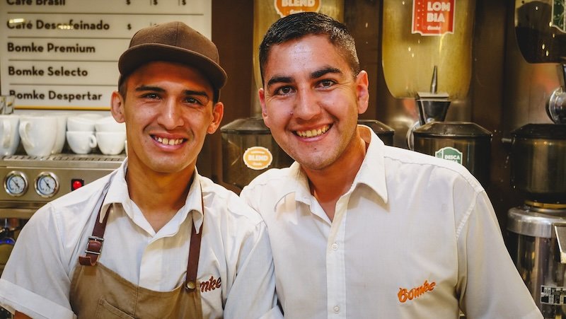 Two smiling employees at Bomke café in Puerto Madryn, Patagonia, standing behind the counter ready to serve coffee and ice cream, reflecting the warm hospitality and inviting atmosphere that makes this local spot a traveler favorite
