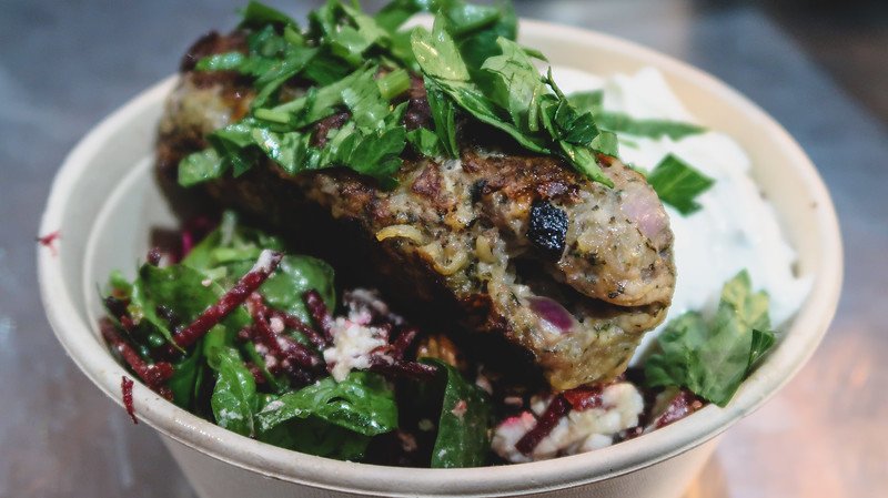 Close-up of a Gourmet Goat kofte bowl at Borough Market in London, featuring grilled spiced meat topped with fresh herbs, served alongside salad greens, beetroot, and creamy yogurt, highlighting the vibrant flavors of this market favorite