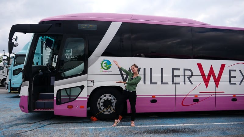 Bus travel is cheap with That Backpacker Audrey Bergner posing outside of a Japanese bus as a things to know as a first-timer in Japan