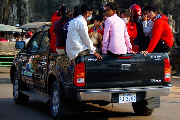 Group of local passengers riding in the open back of a Toyota Hilux pickup truck in Cambodia, illustrating common forms of shared rural transportation near the Temples of Angkor