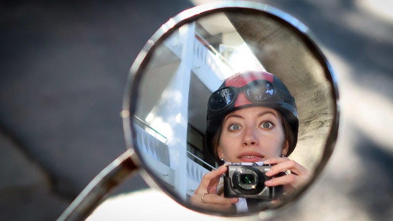 Audrey Bergner of That Backpacker captures a playful biker selfie through the motorcycle mirror during a Cape Peninsula Sidecar Tour from Cape Town to Cape of Good Hope, South Africa. Her helmet, goggles, and camera reflect the excitement of the journey