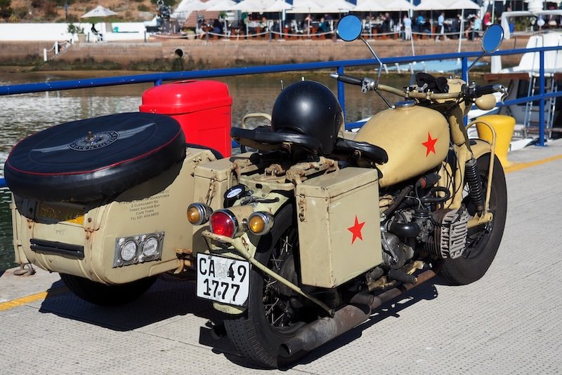 A vintage beige sidecar motorcycle with red stars, black leather seats, and a spare tire mounted on the back, parked on the dock in Simon’s Town during the Cape Peninsula Sidecar Tour in South Africa — a classic ride for coastal exploration