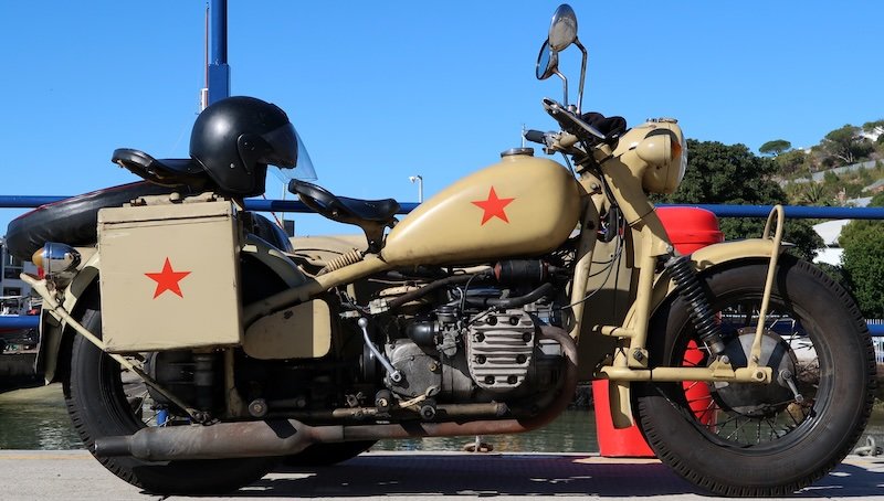 A vintage beige motorcycle with a sidecar, marked with bold red stars, parked under the bright blue skies of Simon’s Town during the Cape Peninsula Sidecar Tour in South Africa — a classic vehicle used for scenic coastal adventures