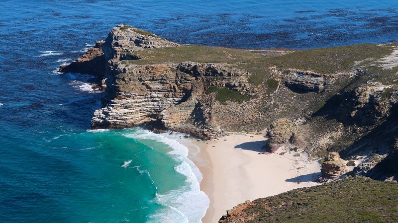 Dramatic aerial view of the rugged coastline, golden sandy beaches, and layered rocky outcrops at Cape Point in South Africa, where turquoise waters meet the cliffs, captured during a scenic Cape Peninsula sidecar tour from Cape Town