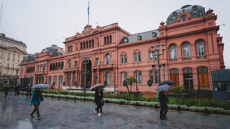 Casa Rosado Pink House on a wet and rainy day in Buenos Aires, Argentina with people out with their umbrellas in full force 