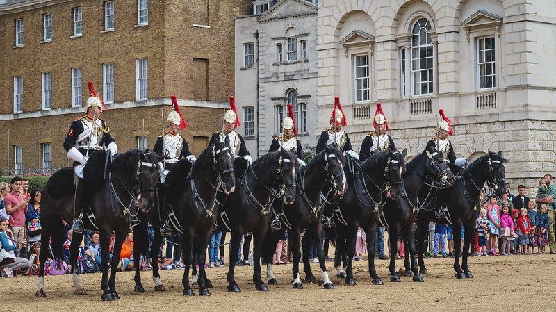 Mounted guards in ceremonial uniforms with polished helmets and red plumes line up on horseback during the Changing of the Guard in London, as crowds of onlookers watch the traditional display of royal pageantry and military precision