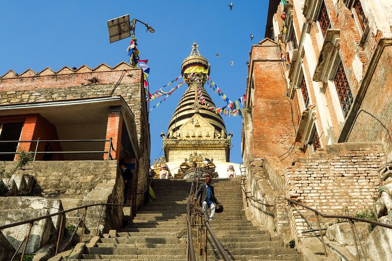 Climb the steep stone steps leading to Swayambhunath, the Monkey Temple in Kathmandu, Nepal, where colorful prayer flags and ancient stupas create a spiritual journey and panoramic views of the city below