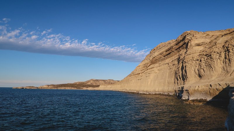 Dramatic coastal cliffs and deep blue waters at Puerto Pirámides on Península Valdés, Argentina, captured in the golden light of late afternoon. This scenic view showcases the region’s striking geology and unspoiled Patagonian coastline