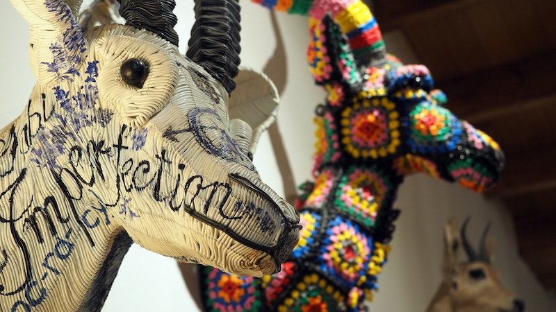Close-up of vibrant African art sculptures of antelope heads in Cape Town, South Africa — one crafted from white recycled materials inscribed with words and another adorned with colorful beadwork patterns, showcasing the city’s creative design scene