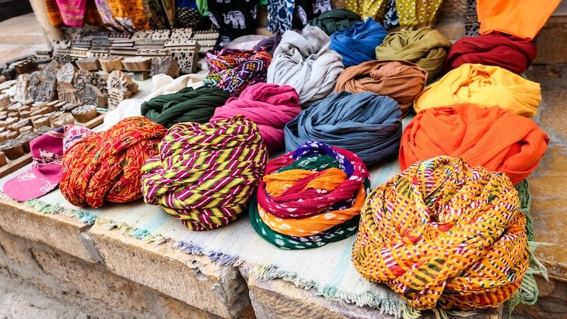 Vibrant turbans and colorful scarves neatly displayed for sale at an outdoor market stall in Jaisalmer, Rajasthan, India, showcasing traditional textiles and local handicrafts
