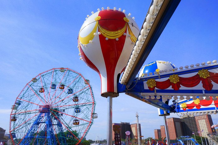 Colorful amusement park rides at Coney Island, New York, featuring the iconic Wonder Wheel Ferris wheel and a vibrant balloon ride under a clear blue sky. This classic Brooklyn destination is famous for its nostalgic boardwalk and seaside fun