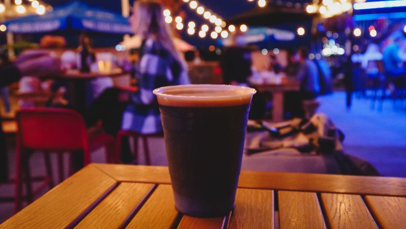 Craft beer at The Stubborn Goat served in a plastic cup placed on a table with nightlife bokeh going on in the background in Halifax, NS